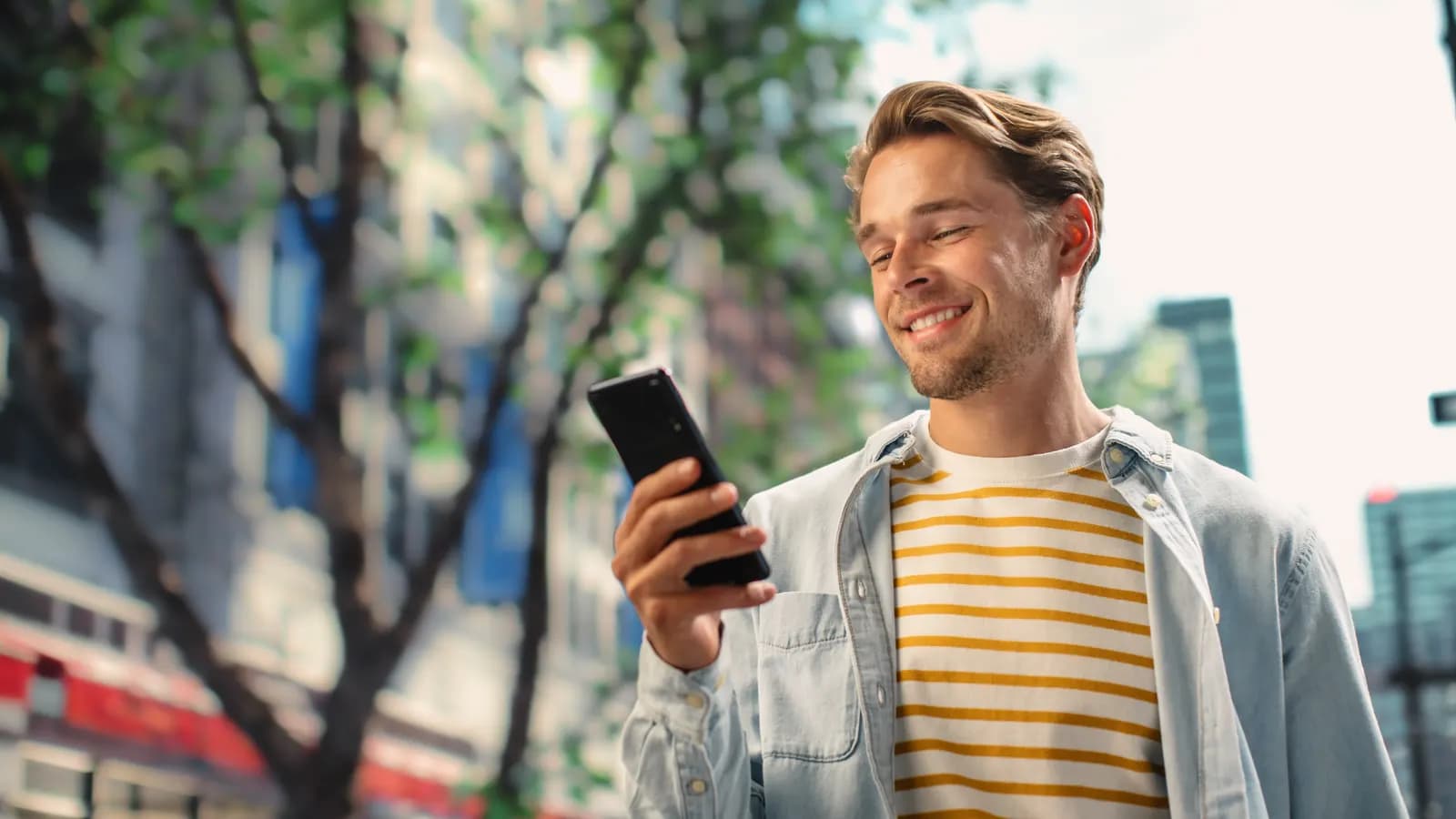 Mosolygó férfi a telefonját nézi a városban
