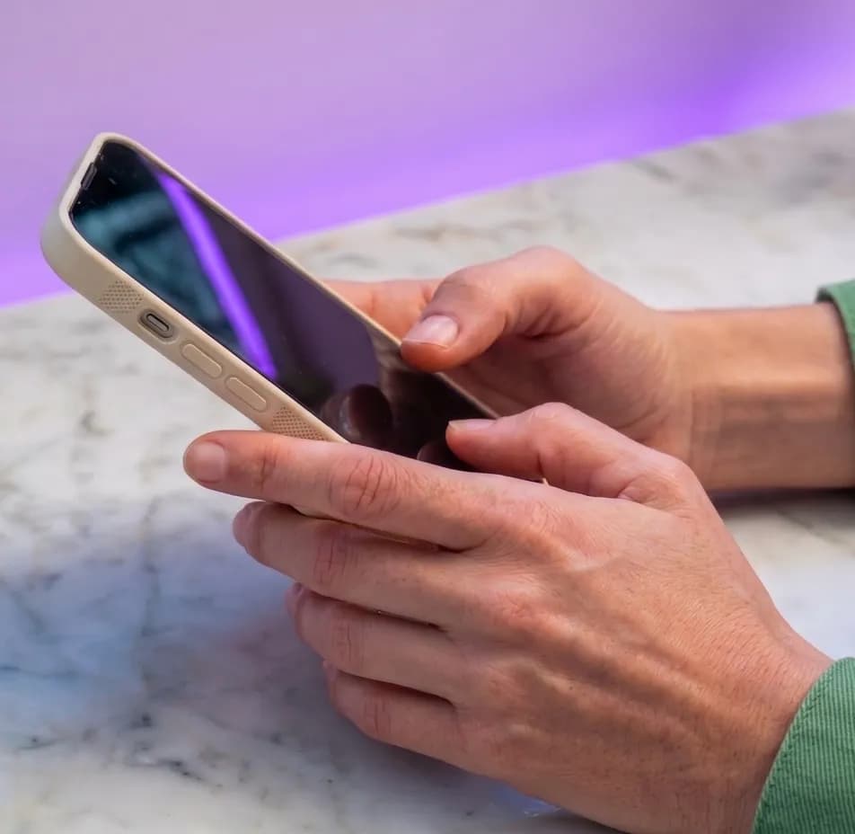 Két kéz mobiltelefont tart egy márványasztal fölött, a háttérben lila fénnyel