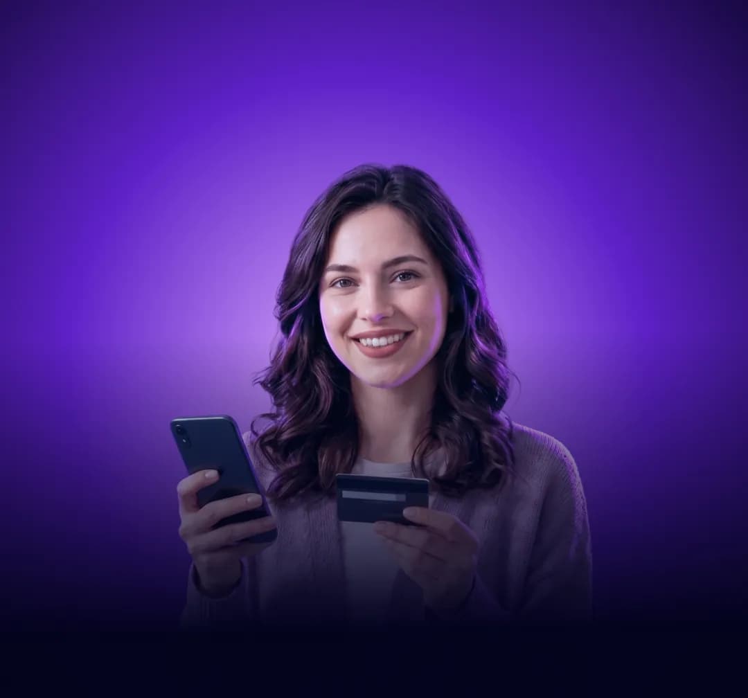 Mosolygó nő, egyik kezében mobiltelefon, másikban bankkártya, lila fényben