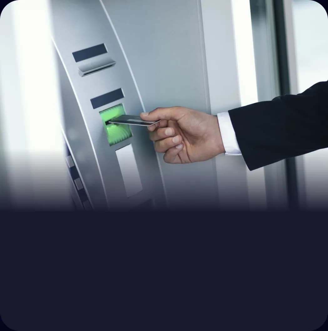 Öltönyös férfi keze bankkártyát helyez egy bankautomata kártyanyílásába.