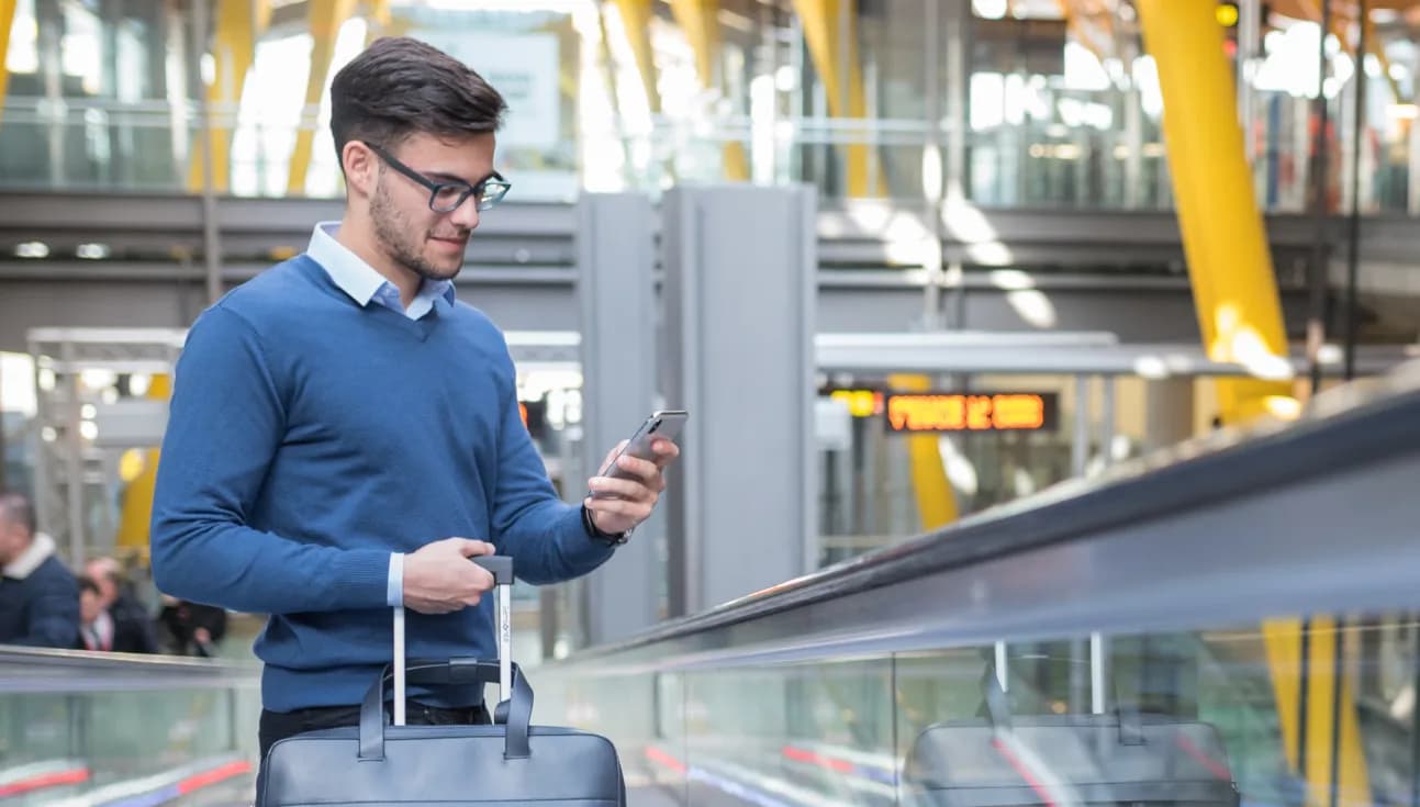 Üzletember gurulós bőrönddel telefonál egy repülőtéren.