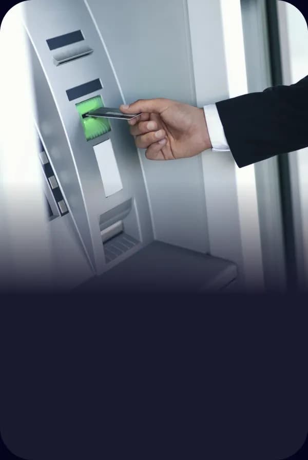 Öltönyös férfi keze bankkártyát helyez egy bankautomata kártyanyílásába.